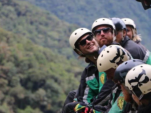 Un grupo de personas con cascos y gafas de sol sentadas y sonriendo al aire libre.