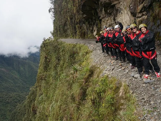 Un grupo de personas con cascos y chaquetas a juego está de pie en un sendero estrecho de montaña.