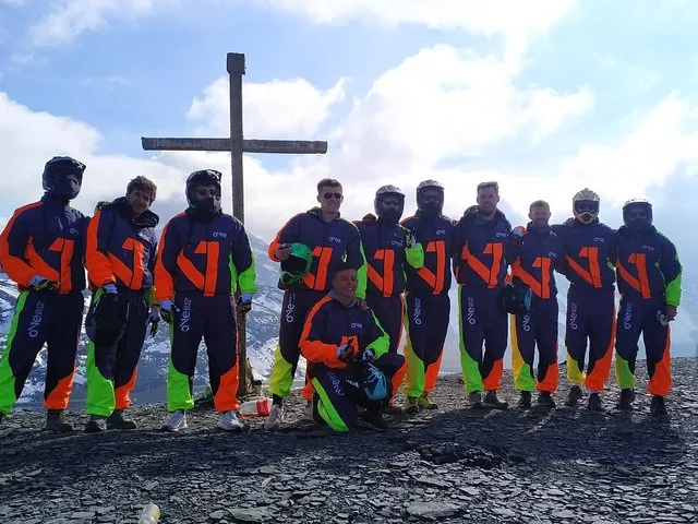 A group of people wearing matching jackets and helmets pose in front of a wooden cross.